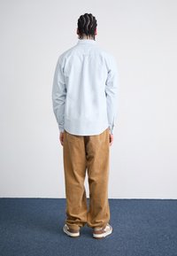 Light blue button-up shirt, relaxed fit, cotton fabric; paired with brown corduroy wide-leg pants and beige sneakers.
