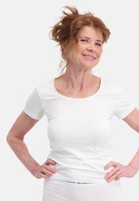 Witte T-shirt met korte mouwen van zachte stof, met een ronde hals. Model staat met handen op de heupen tegen een effen achtergrond.