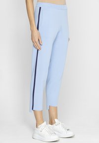 Jasnoniebieskie spodnie 3/4 z granatowymi paskami po bokach, o gładkiej fakturze i elastycznym pasie, w połączeniu z białymi sneakerami.