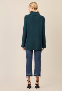 Maglione lavorato a maglia in verde acqua con colletto alto, texture a coste e maniche lunghe, abbinato a jeans con orlo sfilacciato e sandali neri con tacco alto.