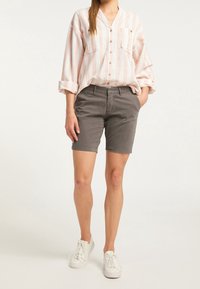 Camisa de botones a rayas rosa claro y blanca con dos bolsillos en el pecho, combinada con pantalones cortos grises y zapatillas blancas.