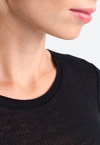 Schwarzes geripptes Rundhals-T-Shirt, Nahaufnahme des Ausschnitts und der Schulterpartie, die glatte Textur und subtile Details ohne Verzierungen zeigt.