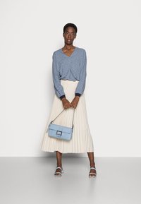 Blusa azul com padrões e decote em V, saia midi plissada branca, bolsa azul clara e sandálias azuis com tiras. Texturas suaves e design elegante.