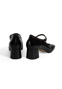 Schwarze Lacklederschuhe mit Absatz, spitzer Zehenpartie, Knöchelriemen und blockförmigem Absatz. Glatte Oberfläche mit minimaler Gestaltung.