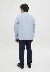 Hele sinine pikkade varrukatega särk nööpidega mansettides, lahvaks sobivuseks. Kantud tumesiniste pükste ja mustade kingadega, nähtud seljast. Minimalistlik disain.