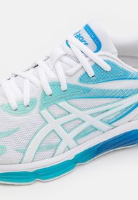 Chaussure de course Asics blanche et turquoise avec empeigne en mesh, lacets blancs, logo détaillé et semelle intermédiaire bleue.
