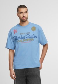 Gaiši zils kokvilnas T-krekls ar īsām piedurknēm, kurā ir "Market Studios California" grafika, apaļa kakla izgriezums un mīksta tekstūra.