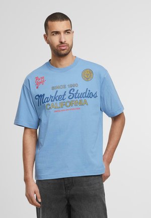 Light blue cotton t-shirt with short sleeves featuring "Market Studios California" graphic, round neckline, and soft texture.