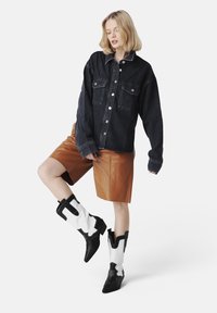 Jachetă din denim cu două buzunare pe piept, pantaloni scurți plisati maro și cizme de cowboy alb-negru cu vârfuri ascuțite și cusături decorative.