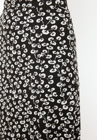 Sorte stof med et hvidt blomstermønster, der har små blade og ranker, tekstureret med plisseringer og en blød finish.