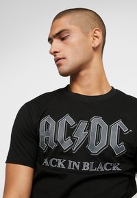 Black cotton t-shirt featuring the "AC/DC" logo in grey, with "BACK IN BLACK" text below, round neckline, and short sleeves.