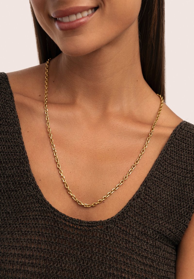 Collar de cadena de oro con eslabones entrelazados, llevado sobre un suéter de punto oscuro con un escote amplio, resaltando el brillo y el diseño de la cadena.