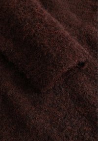 Tmavě hnědý chlupatý vlněný rukáv svetru s viditelnými měkkými, kudrnatými vlákny a texturovanou pleteninou.