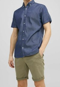 Košile s krátkým rukávem zapínaná na knoflíky z tmavého denimu s límečkem; doplněná o zastrčené khaki kraťasy. Jemná textura a pohodlný střih.