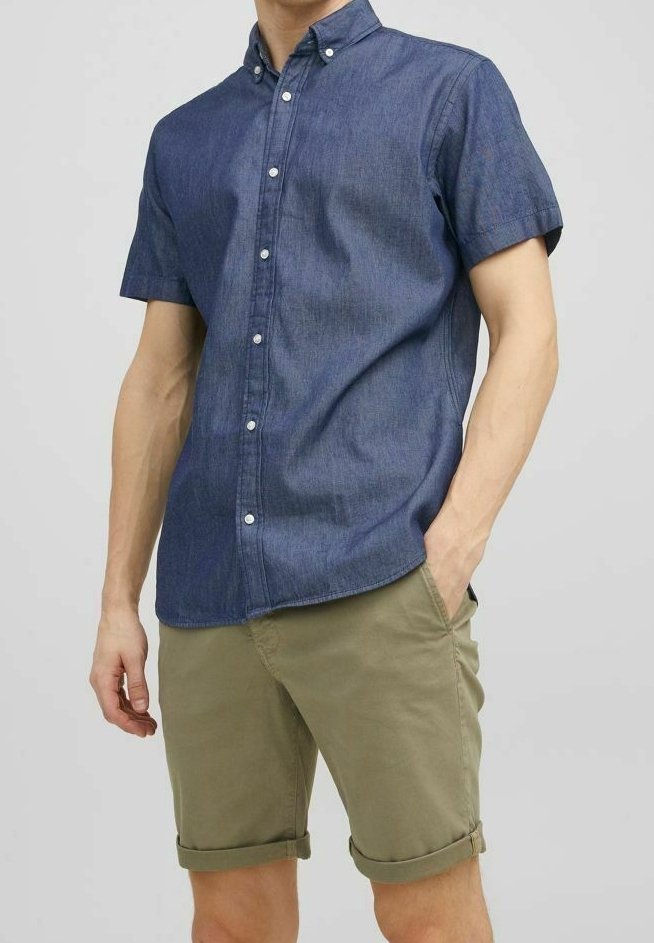 Košile s krátkým rukávem zapínaná na knoflíky z tmavého denimu s límečkem; doplněná o zastrčené khaki kraťasy. Jemná textura a pohodlný střih.