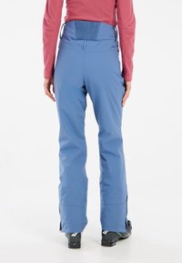 Ski pants in light blue, featuring a high back, elastic waistband, and zippers at the ankles. Pair with black ski boots.