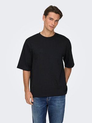 Zwart katoenen T-shirt met korte mouwen, voorzien van een ronde hals en een losse pasvorm. Gecombineerd met lichtblauwe spijkerbroek. Eenvoudig ontwerp, zonder patronen.