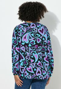 Langarmshirt aus Stoff mit schwarzem Grund und großen, bunten Herzmustern in Lila-, Pink- und Blautönen.