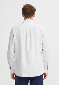 Herren Langarmhemd, hellgrau mit vertikalen Streifen. Mit Knopfmanschetten und Rückenschlitzdetails. Glatte Textur, abgerundeter Saum.
