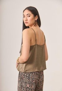 Top sin mangas de satén verde oliva con tirantes ajustables, combinado con pantalones estampados que presentan diseños florales y geométricos en rosa y azul marino.