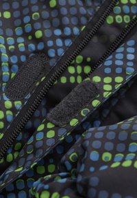 Strukturiertem Stoff mit schwarzem Grund, der ein Muster aus großen blauen und grünen Punkten aufweist. Enthält einen schwarzen Reißverschluss und Klettverschlüsse.