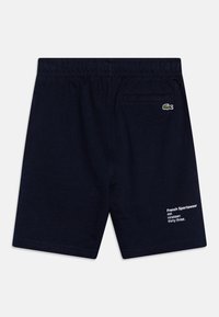 Marina blå shorts i mjukt bomullsmaterial, med resårmidja, bakficka och vit bokstavsdetaljering på sidan.