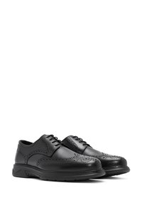 Chaussures en cuir noir avec des détails en brogue, à lacets, à bout rond et semelle en caoutchouc rembourrée. Texture lisse et look classique.