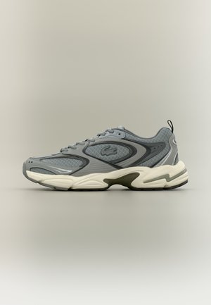 Baskets de sport grises et noires avec des panneaux en mesh, semelle blanche épaisse et logo sur le côté, montrées de profil gauche sur fond clair.