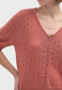 Terrakottafärgad stickad cardigan med V-hals, korta ärmar och broderade bladmönster. Har fem matchande knappar och ribbat avslut.