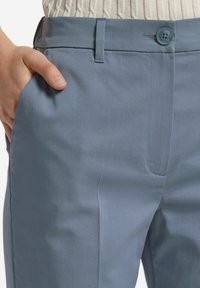 Ljusblå skräddarsydda byxor med en slät, mjuk tyg, framficka och en enkel knappstängning i midjan.