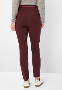 Burgunderfarbene maßgeschneiderte Hose aus einem glatten, dehnbaren Stoff; schlanker Schnitt und ein kontrastierender Bund. Kombiniert mit weißen Sneakers mit einer leichten Sohle.