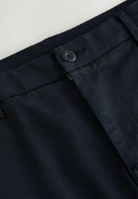 Tmavomodré nohavice s hladkou textúrou, ktoré majú zapínanie na gombík a jemný diagonálny šev pozdĺž pásu.