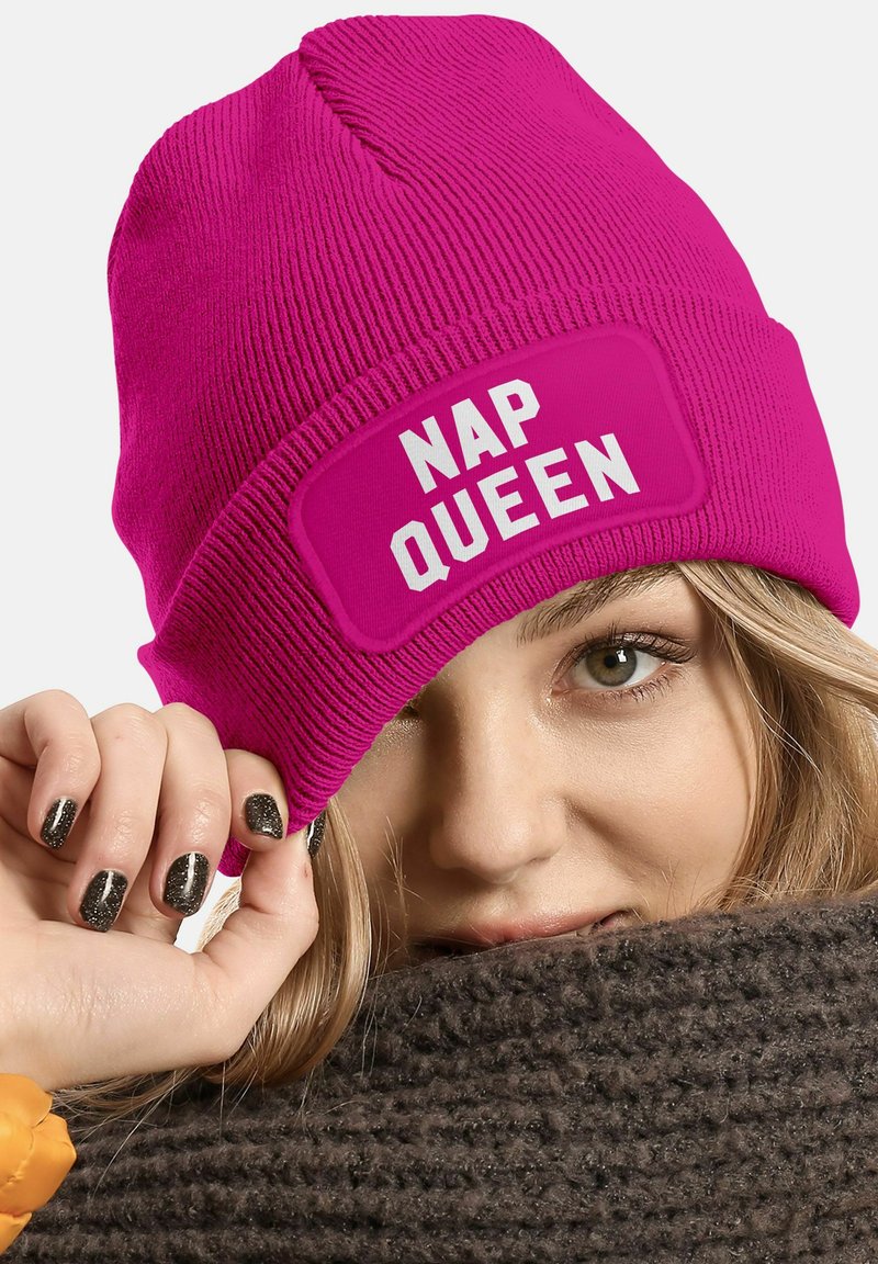 Fuchsia knit beanie featuring a rectangular white patch with "NAP QUEEN" text. Ribbed texture and snug fit.