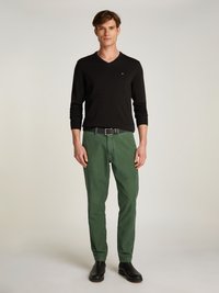 Fekete, hosszú ujjú, vnyakú pulóver, zöld, tapered nadrág, fekete öv, sima textúrával. Fekete bokacsizma teszi teljessé az öltözéket.