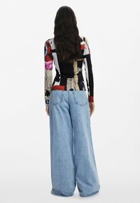 Dug ruko s majicom s raznobojnim mješovitim uzorkom, uparenim s širokim svijetloplavim trapericama s minimalnim šavovima i džepovima.