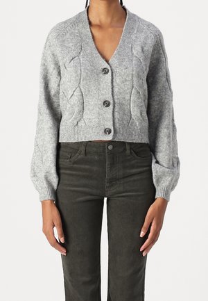 Cardigan gris en tricot avec motif torsadé et boutons, porté avec un pantalon en velours côtelé vert olive foncé.