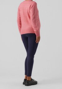 Rosa Wollmischung Pullover mit geripptem Saum, kombiniert mit engen marineblauen Leggings und schwarzen Sneakers, von hinten betrachtet. Einfaches, minimalistisches Design.