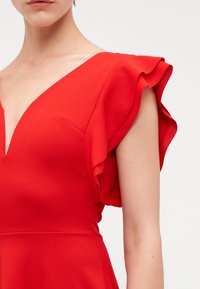 Robe rouge avec un décolleté en V profond et des manches courtes froncées. Fabriquée en tissu lisse avec une silhouette ajustée.