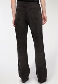 Czarne dżinsy o wysokim stanie ze zwężanym fasonem i subtelną strukturą, z dwiema tylnymi kieszeniami, przedstawione z tyłu.