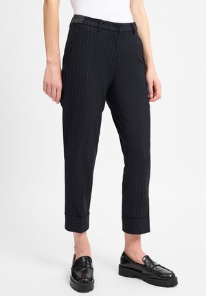 Slim-fit black pinstripe trousers with cuffed hems worn with black chunky loafers on a person standing.