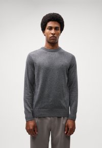 Grå ullkrage-sweater med långa ärmar, ribbade manschetter och nederkant, bärs över ljusgrå byxor. Minimalistisk design, inga synliga mönster eller logotyper.