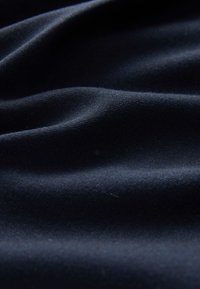 Tengerészkék szövet lágy textúrával, gyengéd hullámokkal és redőkkel, amelyek kiemelik az anyag simaságát és enyhe fényét.