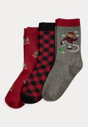 Drei Paar Socken: rot mit Eiskunstlauf-Motiven, schwarz-rot kariert und grau mit einem Eislauf-Bären-Design. Strukturierter Stoff.