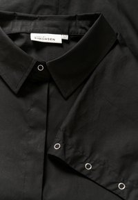 Crna majica sa strukturiranim kragnom, glatka pamučna tkanina, srebreni detalji na rukavu i etiketa na kojoj piše "KAREN BY SIMONSEN."