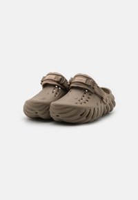 Brown molded clogs with a textured finish, featuring ventilation holes, a flat sole, and an adjustable strap across the instep.