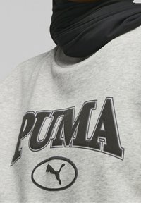 Felpa grigia con stampa e logo "PUMA" neri in un ovale. Il materiale sembra morbido e di texture, con un colletto rotondo. Accessorio nero visibile attorno al collo.