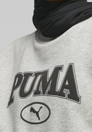 Grå sweatshirt med svart "PUMA"-tryck och logotyp i en oval. Materialet ser mjukt och texturerat ut med en rund halsringning. Svart halsaccessoar synlig.