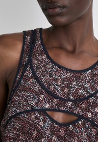 Haut à motif floral avec bordures en marine courbées, présentant des détails découpés. Le tissu a une texture douce avec des accents rouges, blancs et noirs.