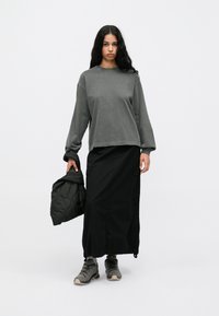 Szary długi sweter z luźnym krojem, połączony z czarną spódnicą cargo do kostek. Modelka trzyma puchową czarną kurtkę.