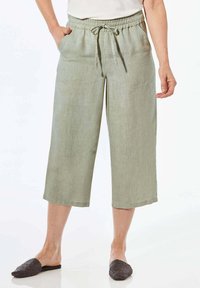 Helle grüne Leinen-Culottes mit einem elastischen Bund, Kordelzug und seitlichen Taschen, die knapp unter dem Knie enden. Flache, strukturierte schwarze Slipper.